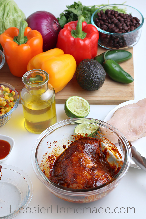 chicken in seasonings in clear glass bowl with toppings for burrito bowl recipe