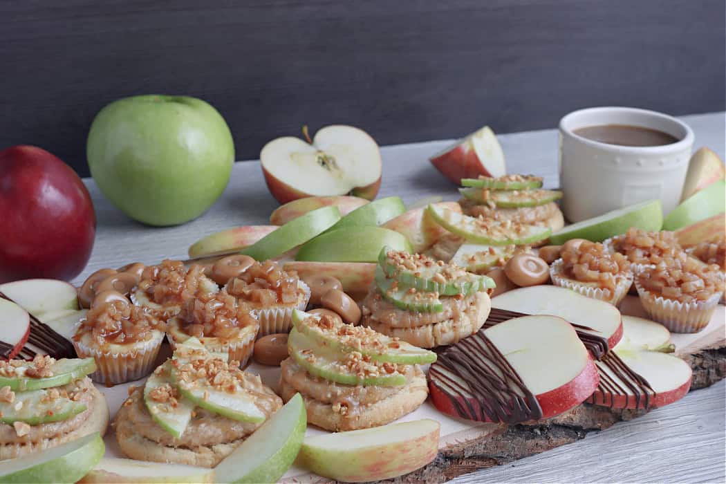 wooden board with caramel apple cookies, apples, caramel sauce, candy and more