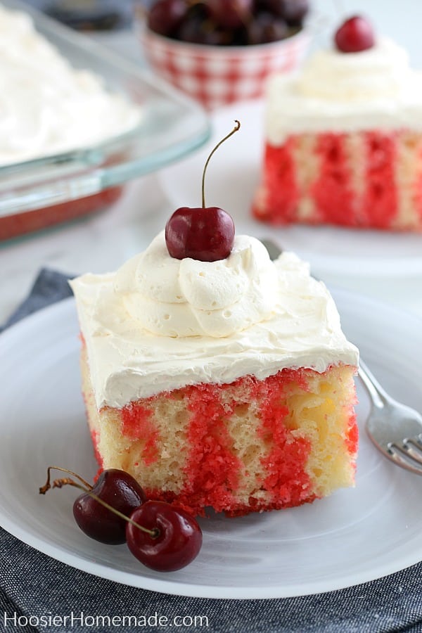 A cherry topped cake on a whte plate with cherries and a fork